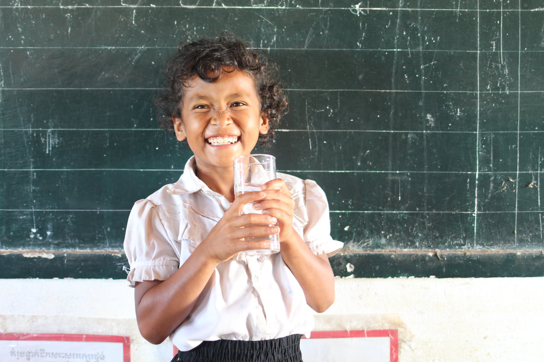 A young girl smiling while enjoying clean drinking water from Wateroam's portable water filter