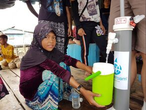 A happy child collecting clean drinking water from a community water filter from Wateroam