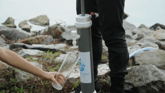 A man operating a community water filter by handpump and collecting clean water