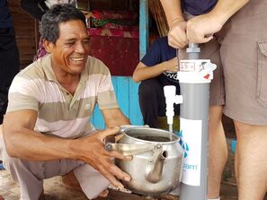A happy, middle-aged man obtaining improved drinking water from a community water filter