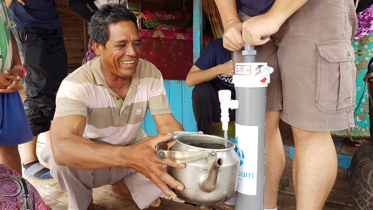 A happy man collecting improved drinking water from a community water filter, the ROAMfilter™ Plus